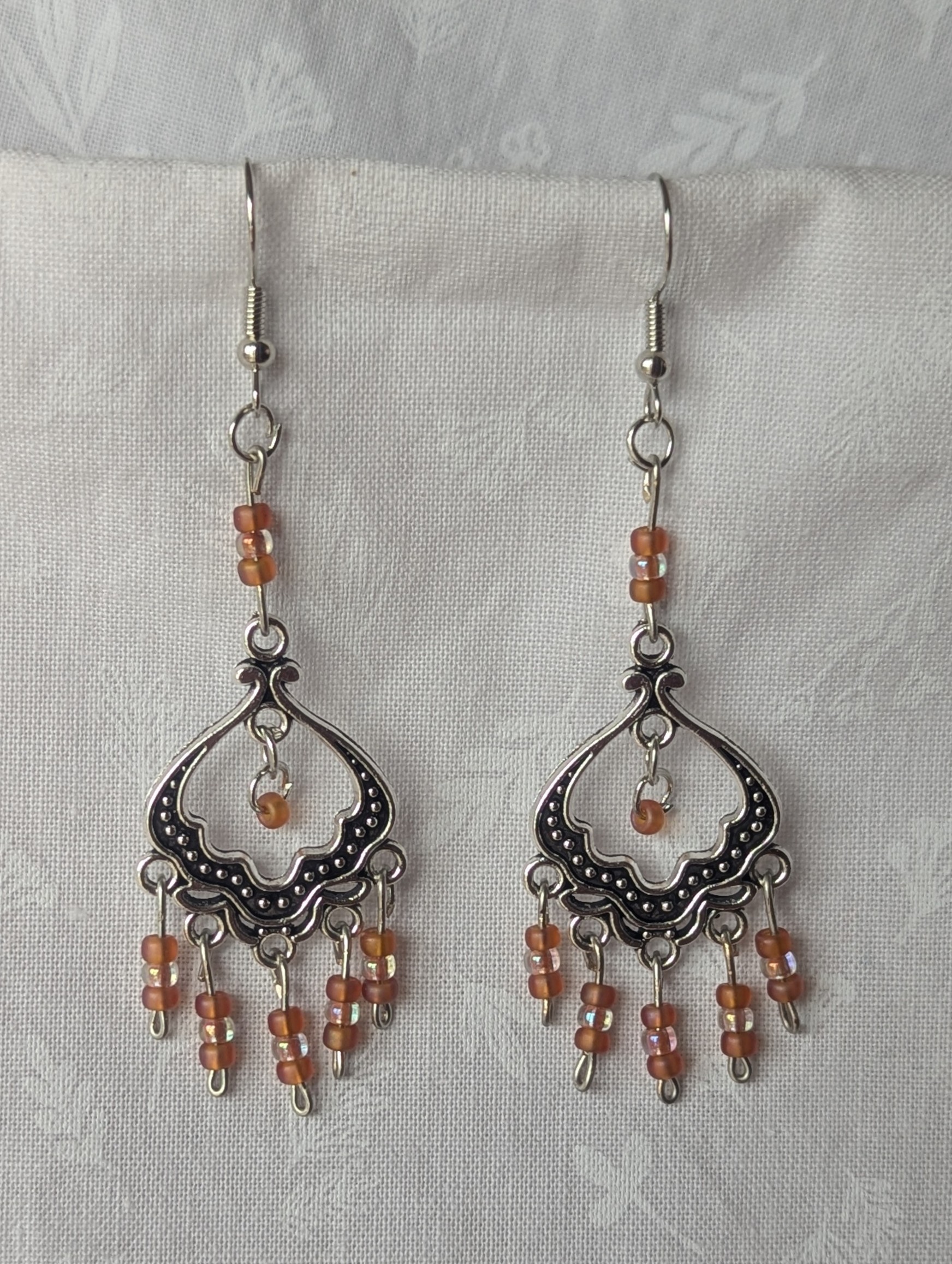Blushing Elegance Chandelier Earrings feature a Tibetan ornament and 19 beads in frosted iridescent ballet pink and pale pink-lined clear.