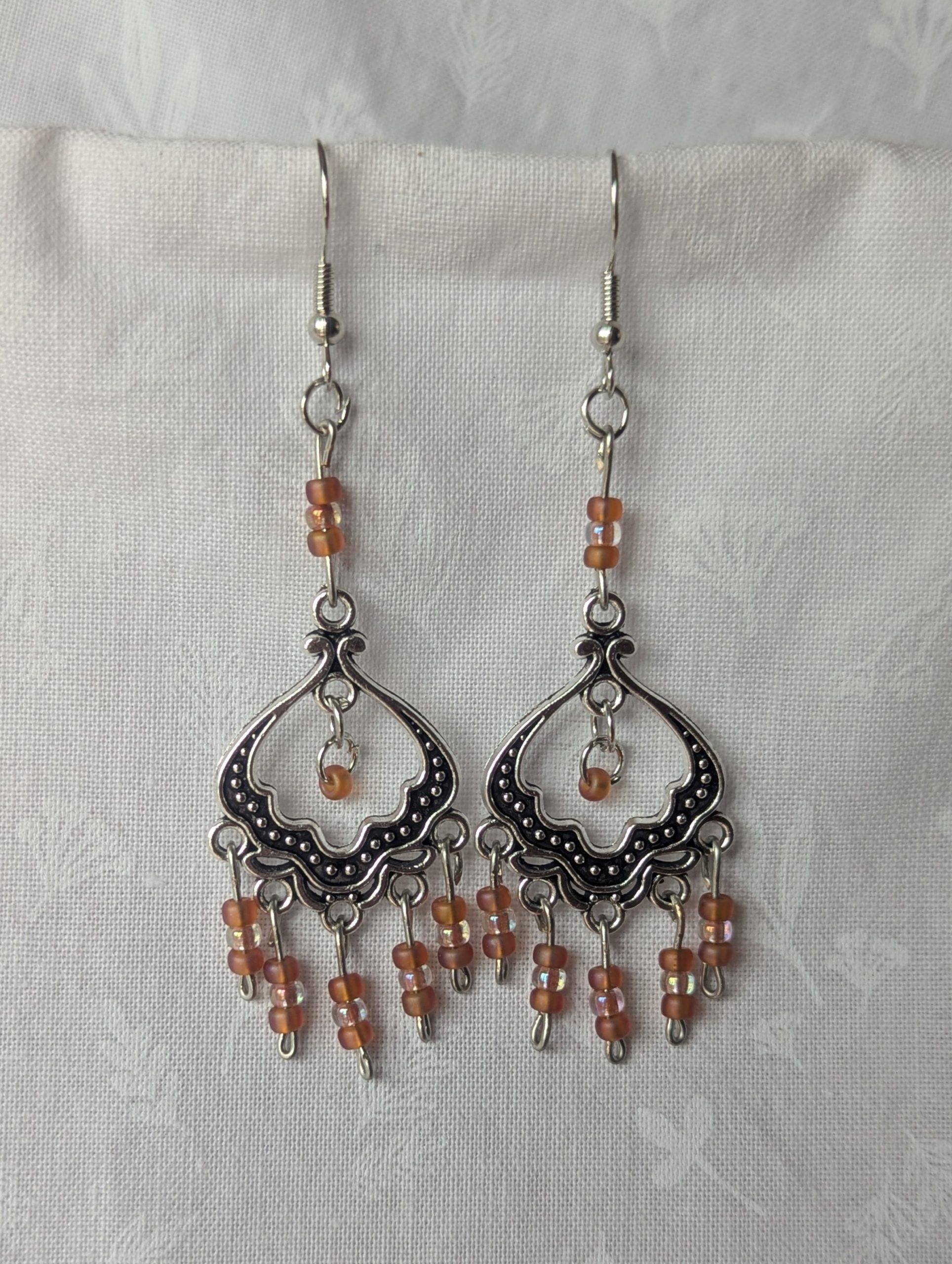 Blushing Elegance Chandelier Earrings feature a Tibetan ornament and 19 beads in frosted iridescent ballet pink and pale pink-lined clear.