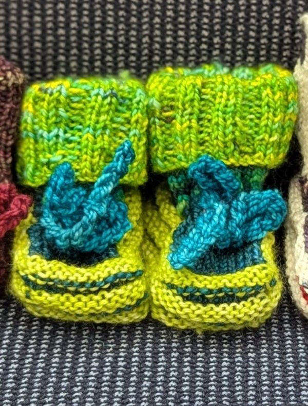 Bright green handknit baby booties with ribbed cuffs and teal blue ties, made from superwash merino wool.