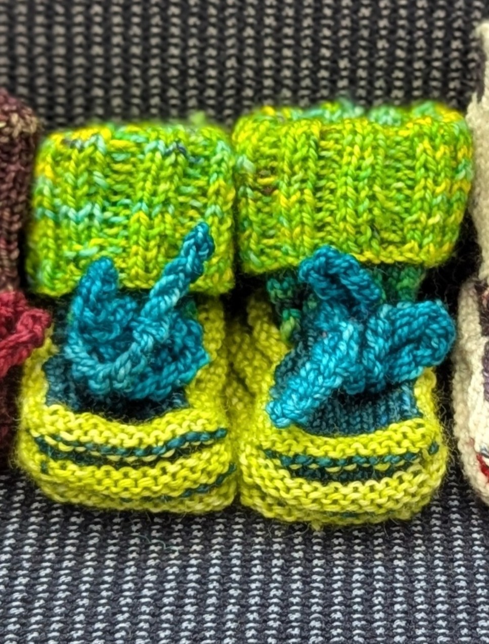 Bright green handknit baby booties with ribbed cuffs and teal blue ties, made from superwash merino wool.