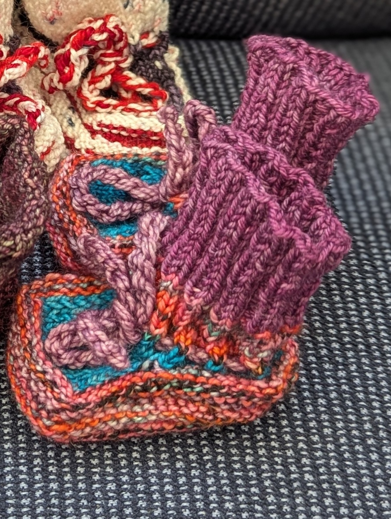 Multicolored baby booties in pink, purple, and turquoise with ribbed cuffs and soft pink ties, handknit for newborns.