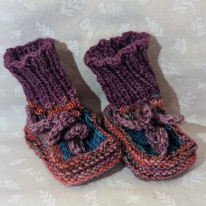 Multicolored baby booties in pink, purple, and turquoise with ribbed cuffs and soft pink ties, handknit for newborns.