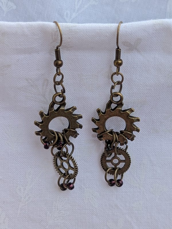 Crimson Cogs Earrings: Steampunk-style earrings with two bronze-colored gears and four silver-lined wine-colored beads, finished with bronze earring hooks.