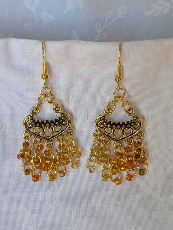 The Golden Hour Cascade Earrings: Pair of chandelier-style earrings with 25 glass beads in five shades and textures of gold, hung from antiqued gold ornaments with gold jump rings.