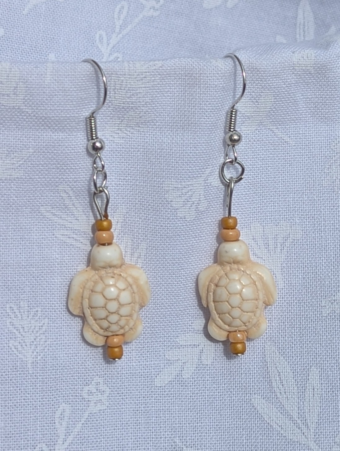 Desert Drift Turtle Earrings: Pair of earrings featuring beige turtle charms with tan and light brown beads on each side, connected by steel-colored findings.