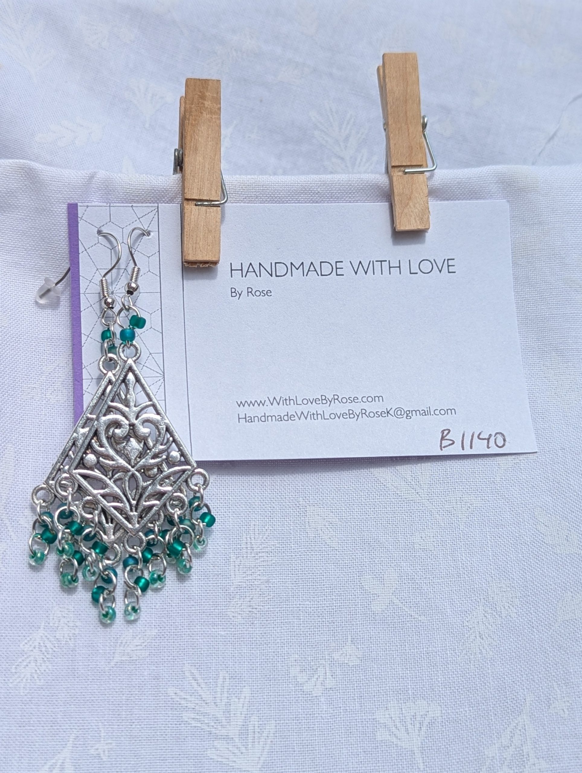 Tideweaver earrings: Silver diamond-shaped filigree earrings with 15 cascading teal beads in frosted, matte, and translucent finishes, plus 2 teal accent beads above each ornament.