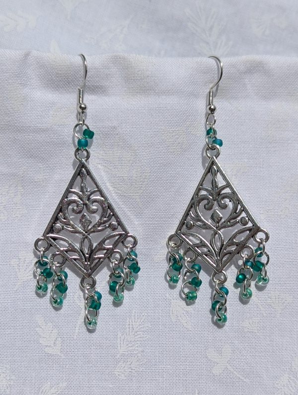 Tideweaver earrings: Silver diamond-shaped filigree earrings with 15 cascading teal beads in frosted, matte, and translucent finishes, plus 2 teal accent beads above each ornament.