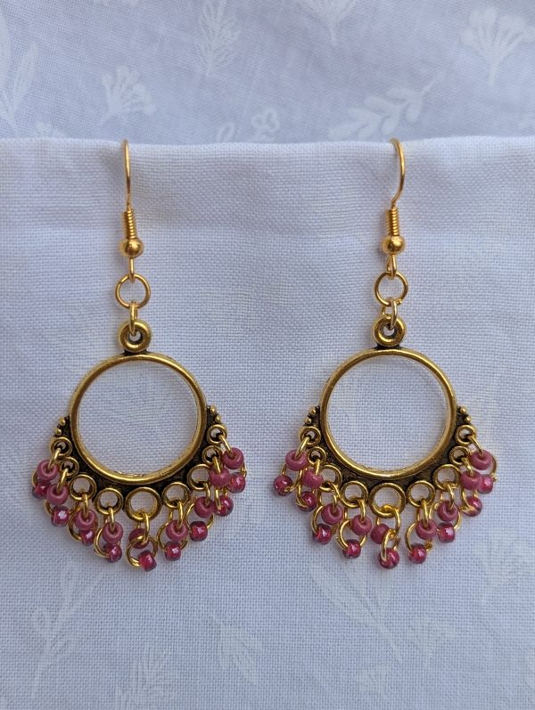 Rosé Reverie Earrings: Antique gold earrings with 18 rose-colored beads—featuring rose-lined clear and solid petal pink—hanging from ornate gold-toned ornaments.