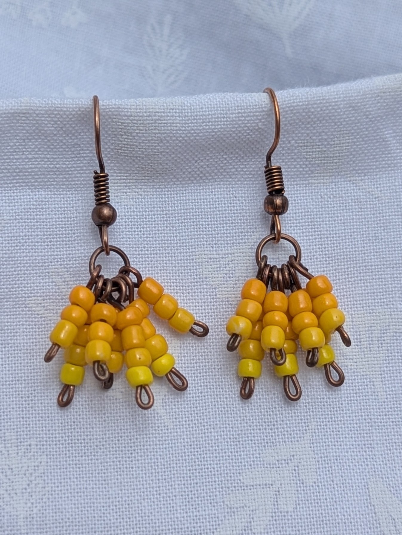 Sunburst Petals Earrings: Yellow beaded earrings with 24 beads in golden tones—marigold, honey, and lemon—hung from bronze posts with matching hooks.