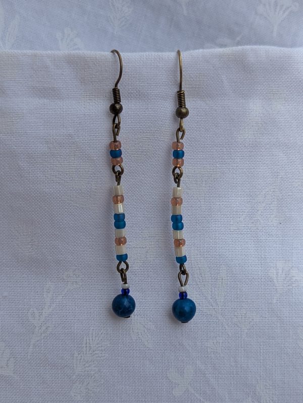 Moonlit Tides Earrings: Drop earrings featuring a capri blue focal bead accented by 14 small pearlescent white, silvery pink, and iridescent blue beads on bronze-colored findings.