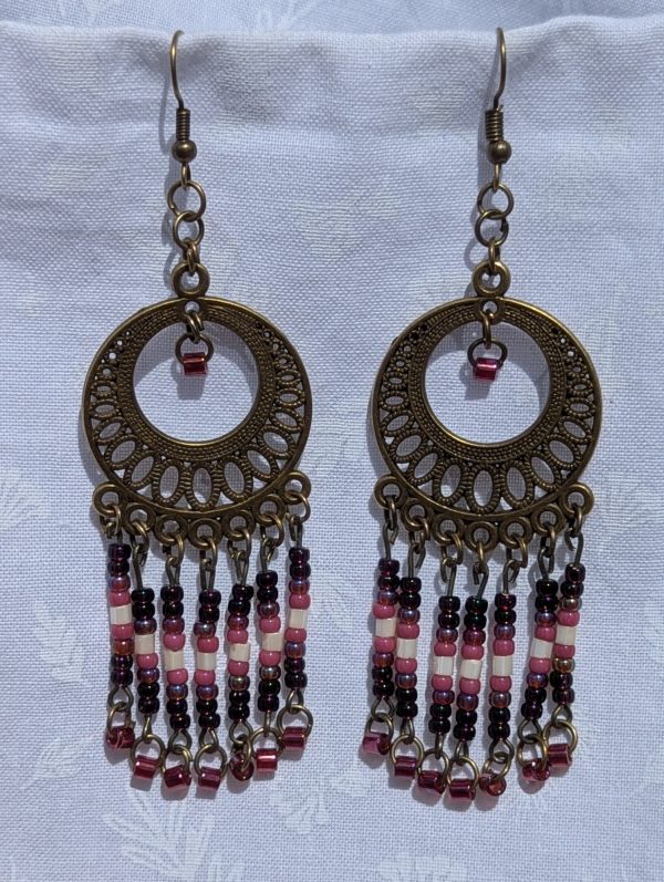 Desert Rose Sundial — Bronze filigree earrings with cascading glass beads in garnet, blush pink, ivory, rose, and crimson, arranged in five vertical strands.