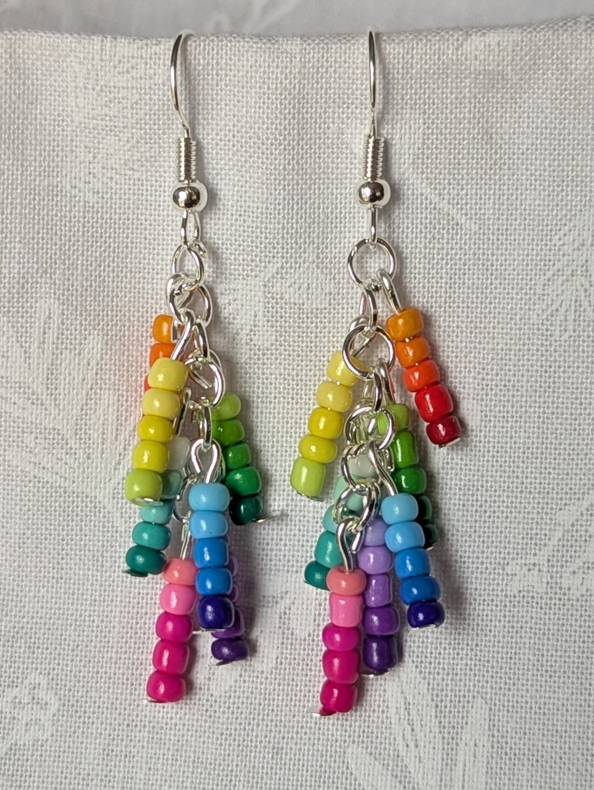 Handmade gradient rainbow earrings featuring 35 colorful seed beads per earring, arranged in 7 soft color gradients and hung from silver-toned posts with silver hooks.
