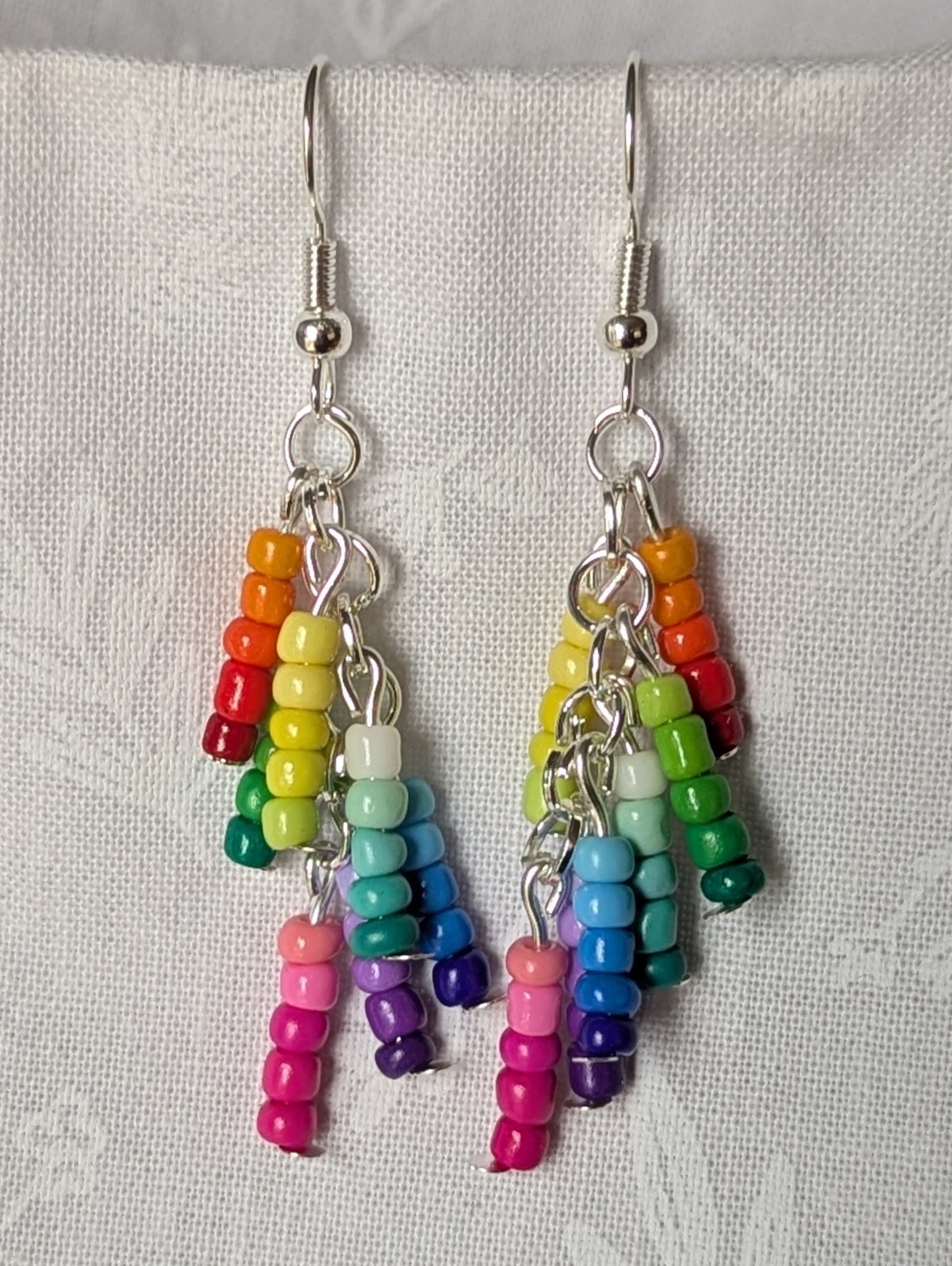 Handmade gradient rainbow earrings featuring 35 colorful seed beads per earring, arranged in 7 soft color gradients and hung from silver-toned posts with silver hooks.