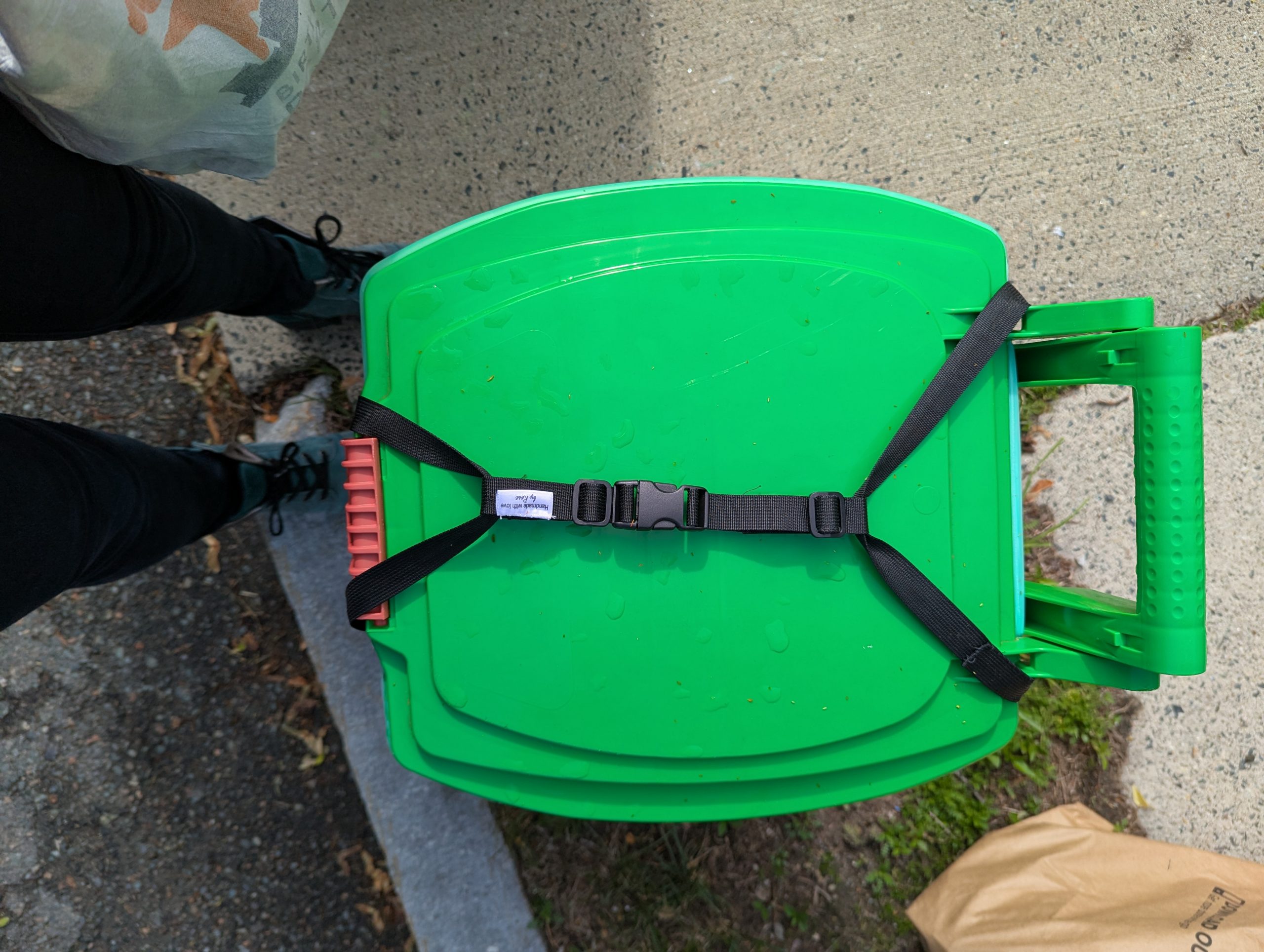 Rodent-Resistant Compost Bin Strap System: Green compost bin secured with black buckle strap system to prevent animal access