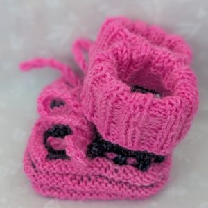 Pink handknit baby booties with blue/black accents, ribbed cuffs, and tied laces, made from soft merino wool for newborns.