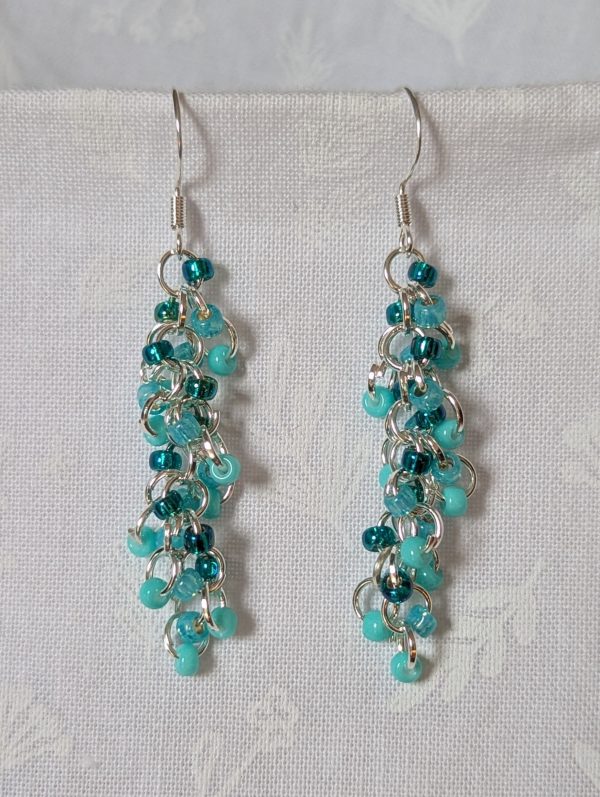 Pair of handmade teal dangle earrings with 27 seafoam, silver-lined teal, and iridescent cyan beads linked by silver rings and sterling silver hooks.