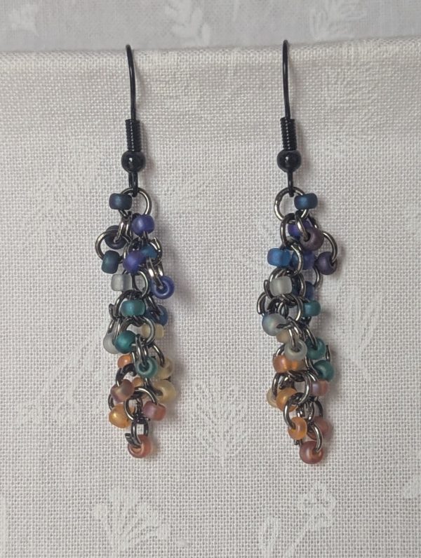 Handmade galaxy-themed earrings with 24 iridescent beads in 8 celestial colors, suspended on tungsten-colored rings with black hooks.