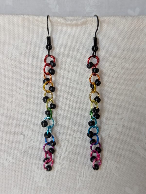 Dark Prism Earrings featuring 13 matte black beads and rainbow-colored jump rings from red to pink, hanging from black earring hooks.