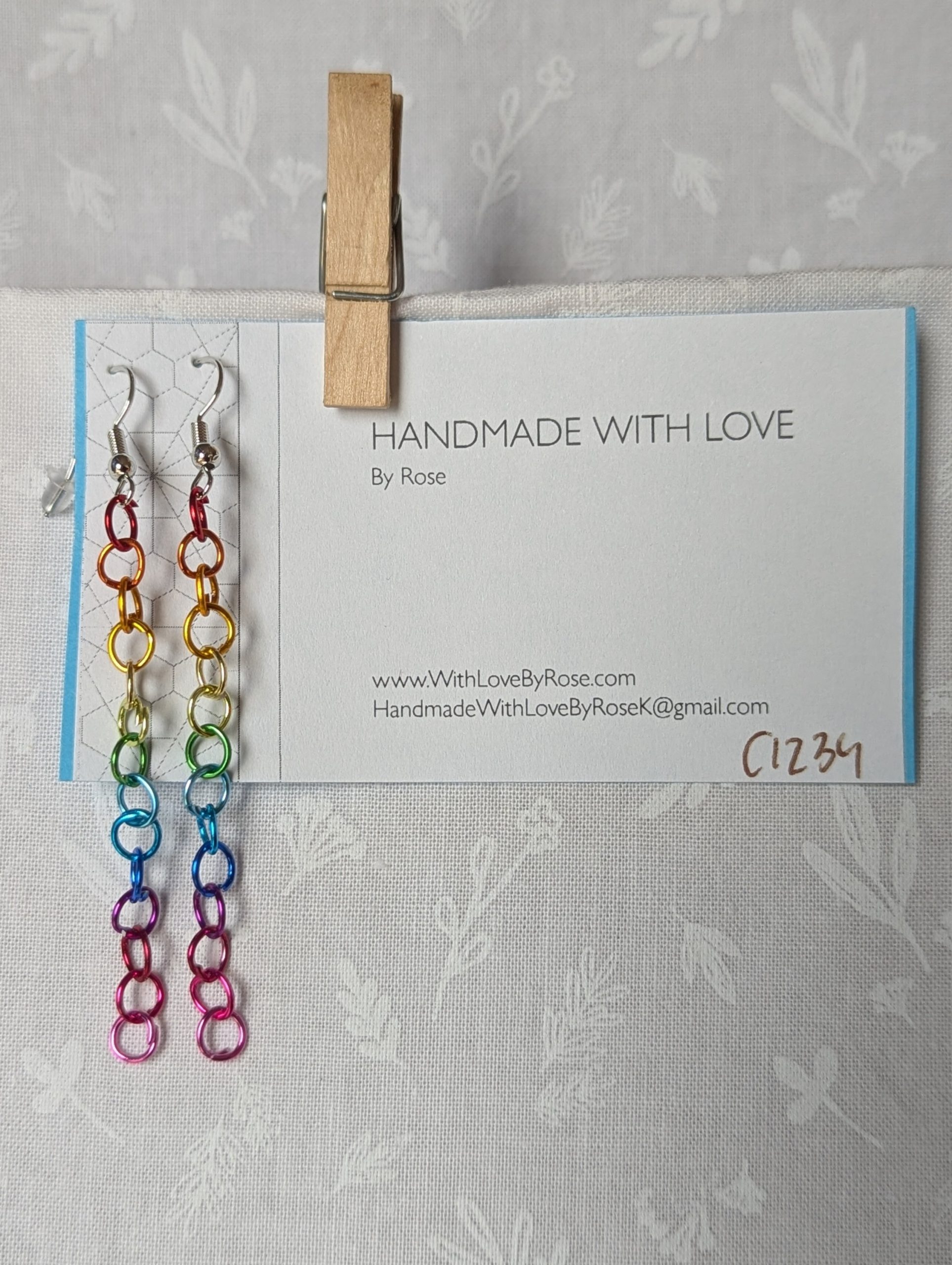 Spectrum Sleek Earrings made with 14 rainbow-colored jump rings, arranged in a smooth gradient and hung from polished steel-colored hooks.