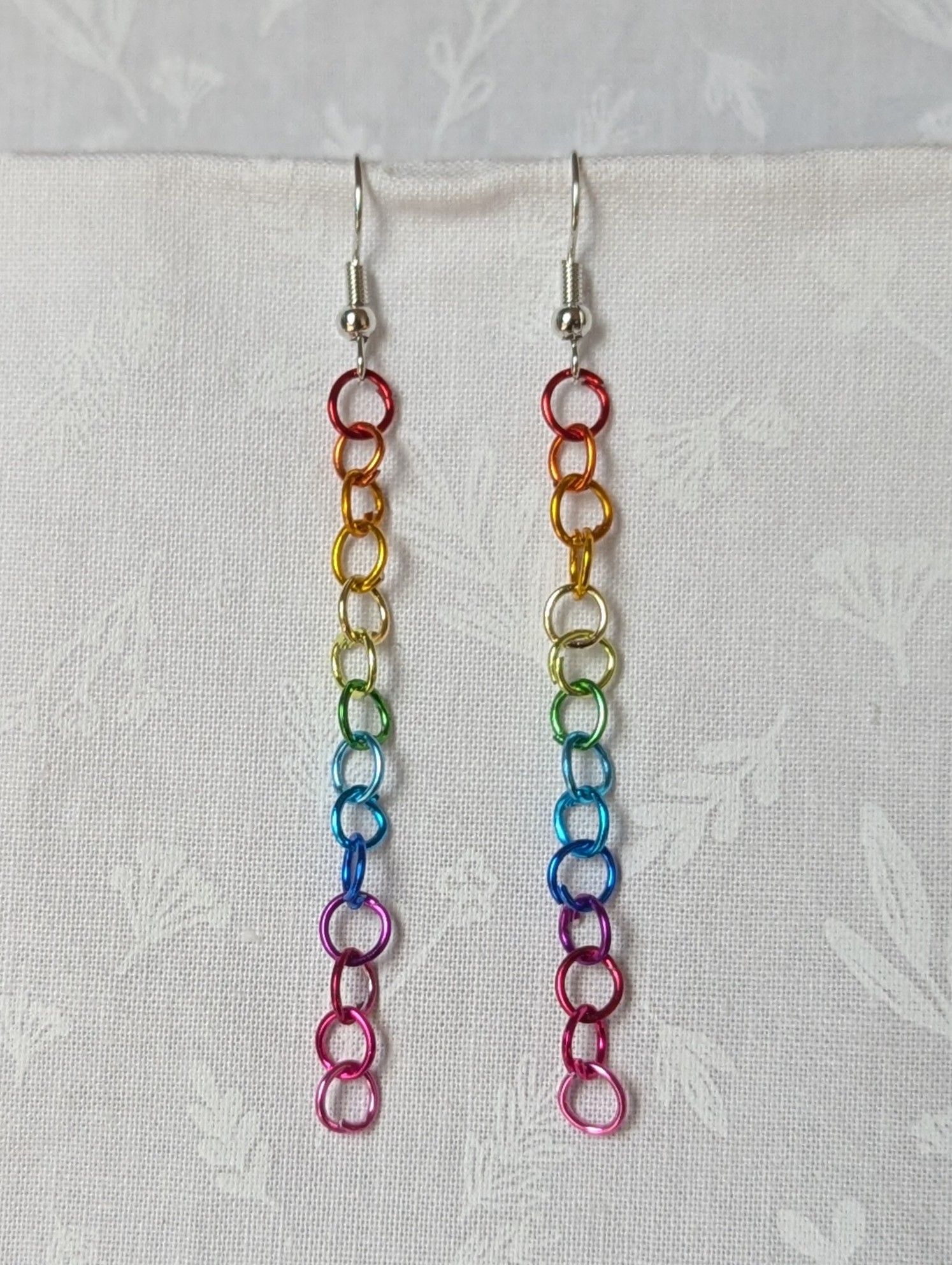 Spectrum Sleek Earrings made with 14 rainbow-colored jump rings, arranged in a smooth gradient and hung from polished steel-colored hooks.