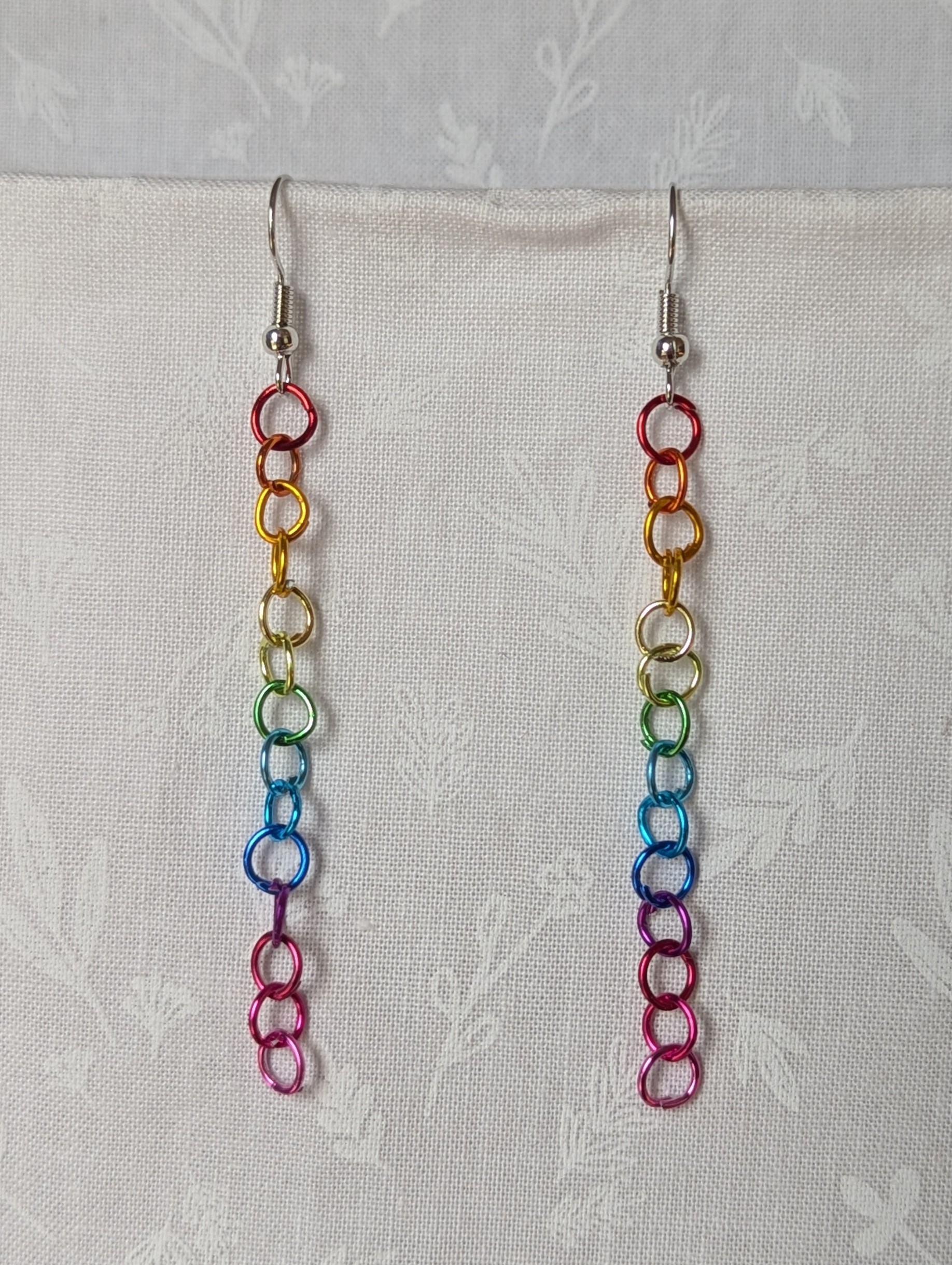 Spectrum Sleek Earrings made with 14 rainbow-colored jump rings, arranged in a smooth gradient and hung from polished steel-colored hooks.