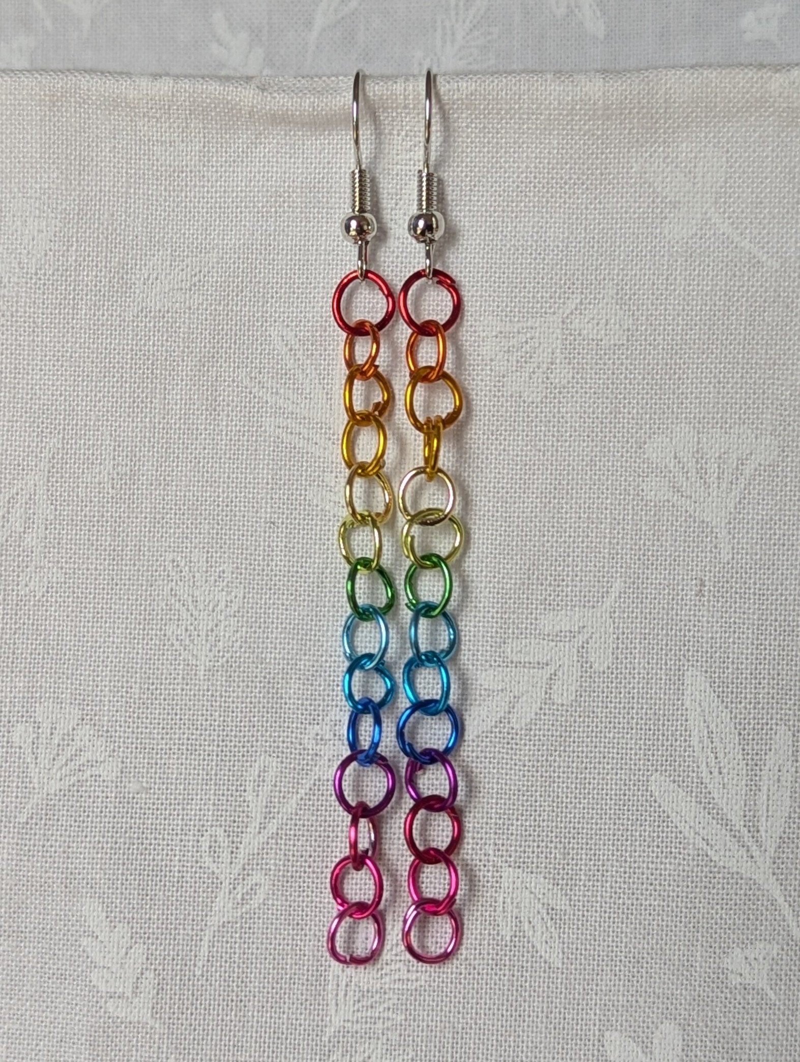 Spectrum Sleek Earrings made with 14 rainbow-colored jump rings, arranged in a smooth gradient and hung from polished steel-colored hooks.