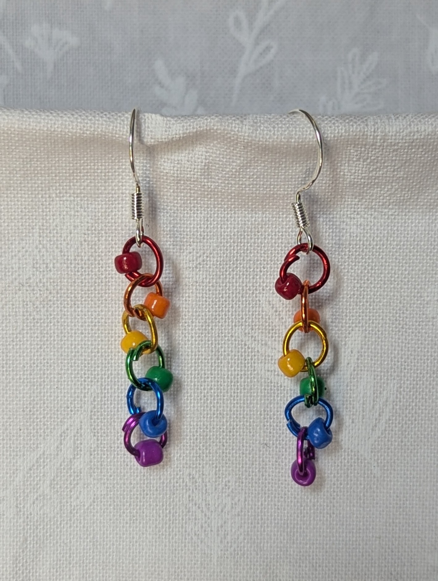 Colorful handmade Rainbow Whimsy Earrings with five bright beads on rainbow gradient jump rings and sterling silver hooks.
