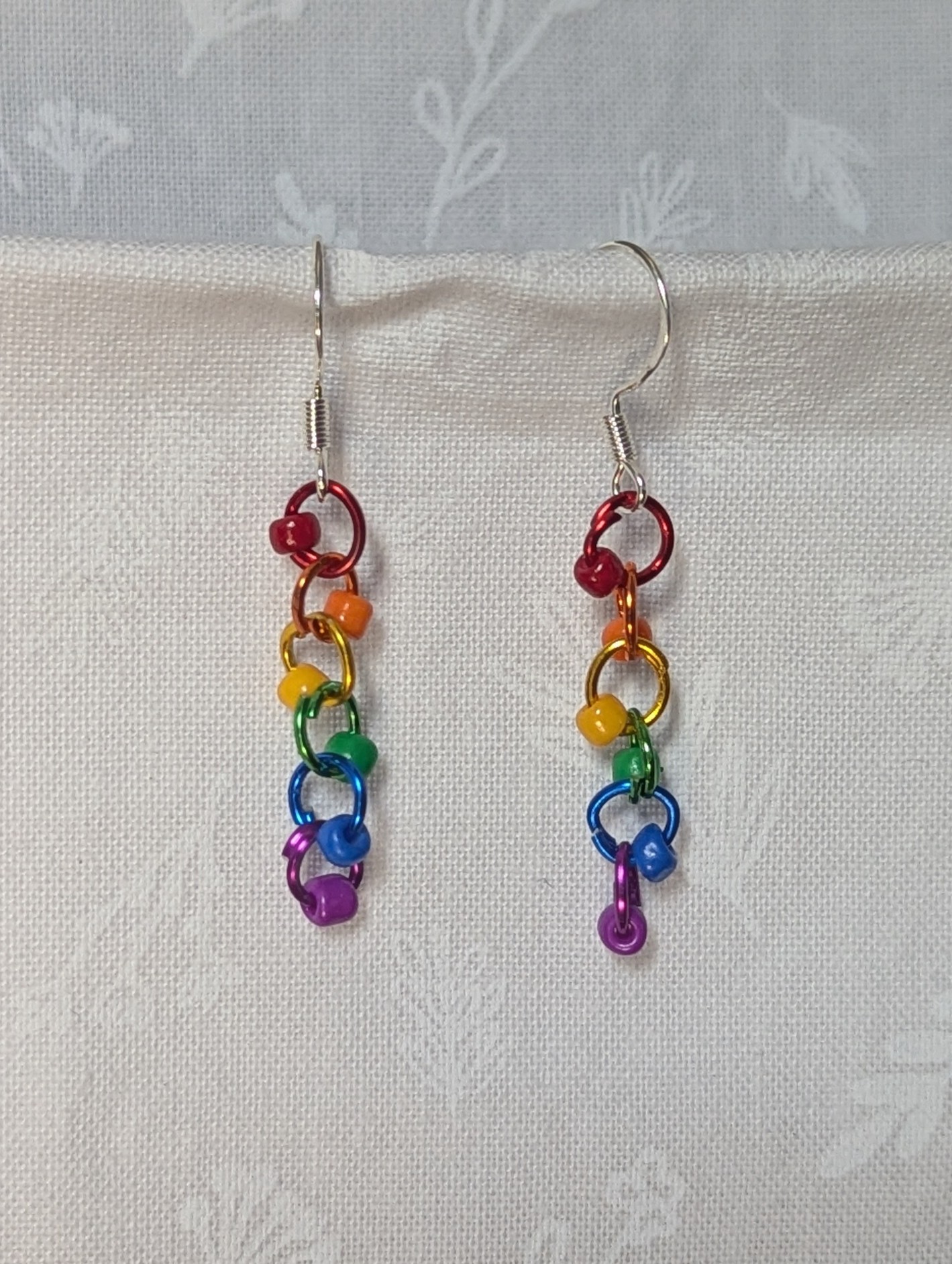 Colorful handmade Rainbow Whimsy Earrings with five bright beads on rainbow gradient jump rings and sterling silver hooks.