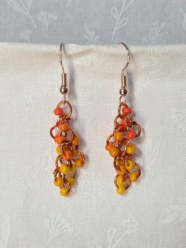 Handmade dangle earrings with 18 orange and yellow glass beads in six warm shades, linked with orange jump rings and rose gold-colored hooks.