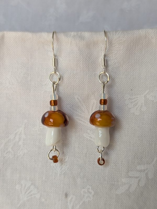 Handmade brown mushroom earrings with glass toadstools, brown and white seed beads, and sterling silver hooks.