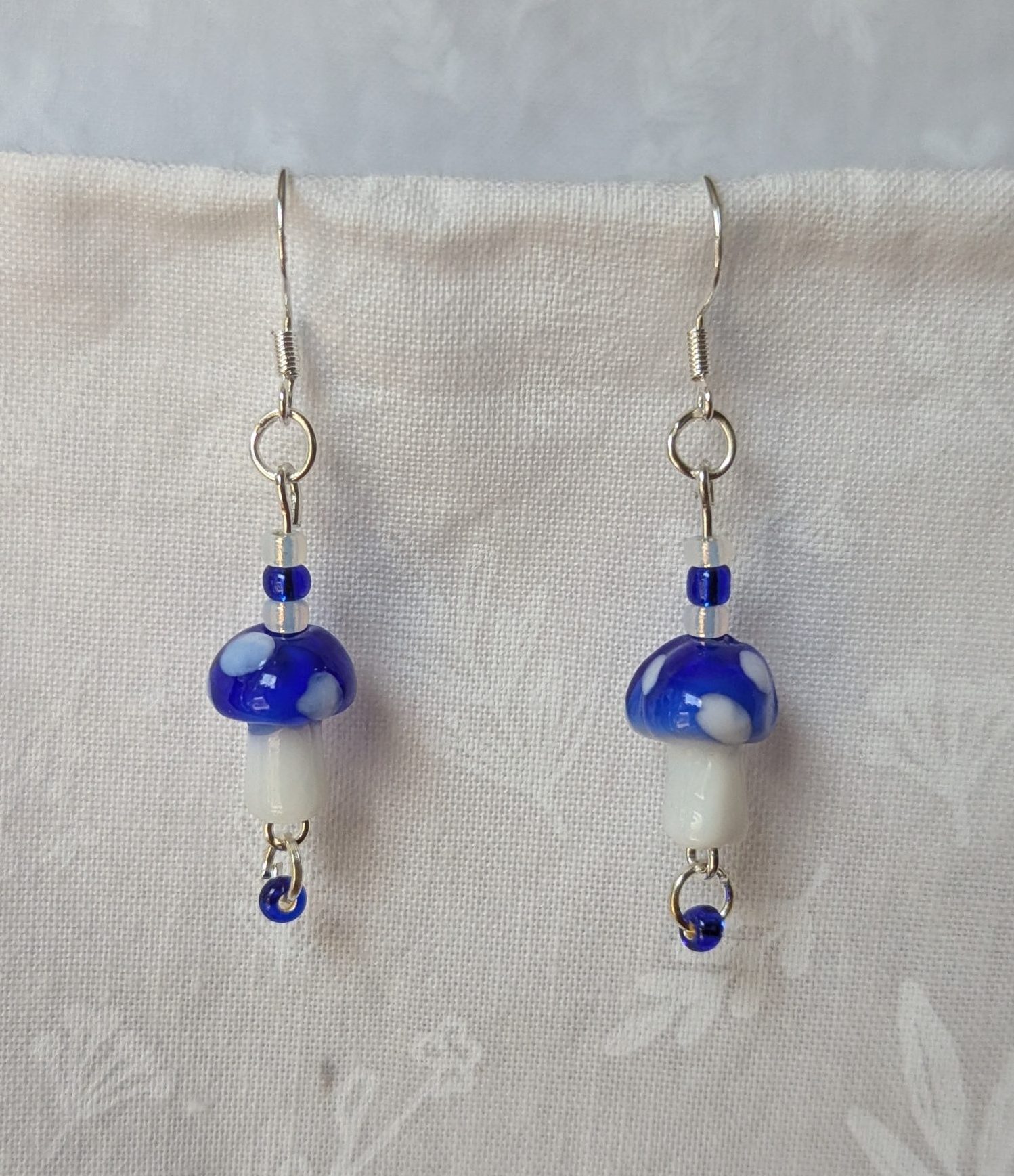 Handmade blue mushroom earrings with glass toadstools, blue and white seed beads, and sterling silver hooks.