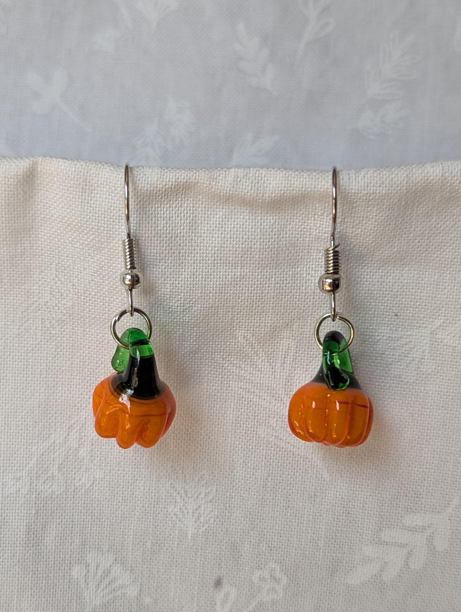 Handmade autumn pumpkin earrings with amber-orange glass pumpkin beads, green accents, and steel-colored findings.