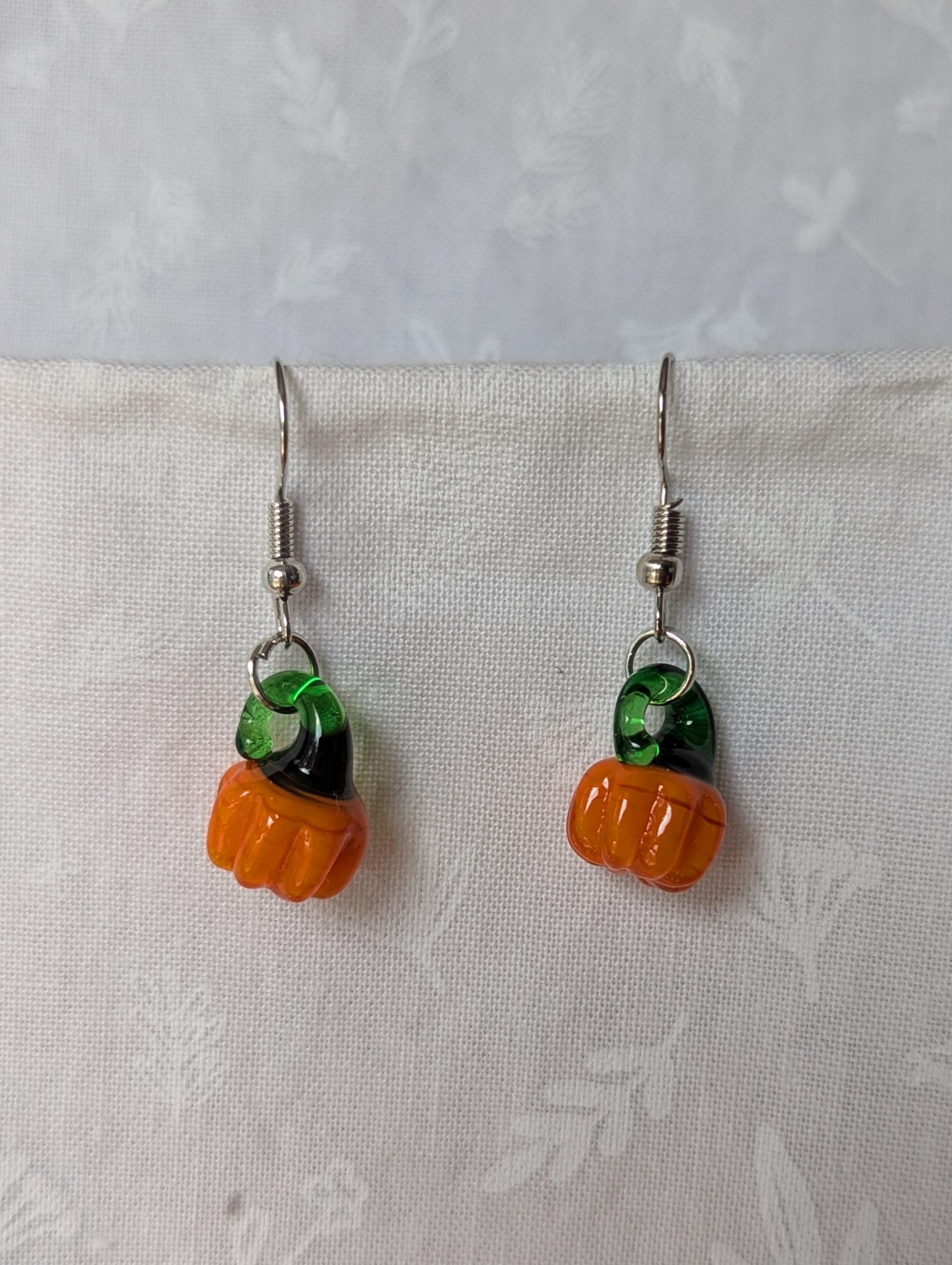 Handmade autumn pumpkin earrings with amber-orange glass pumpkin beads, green accents, and steel-colored findings.