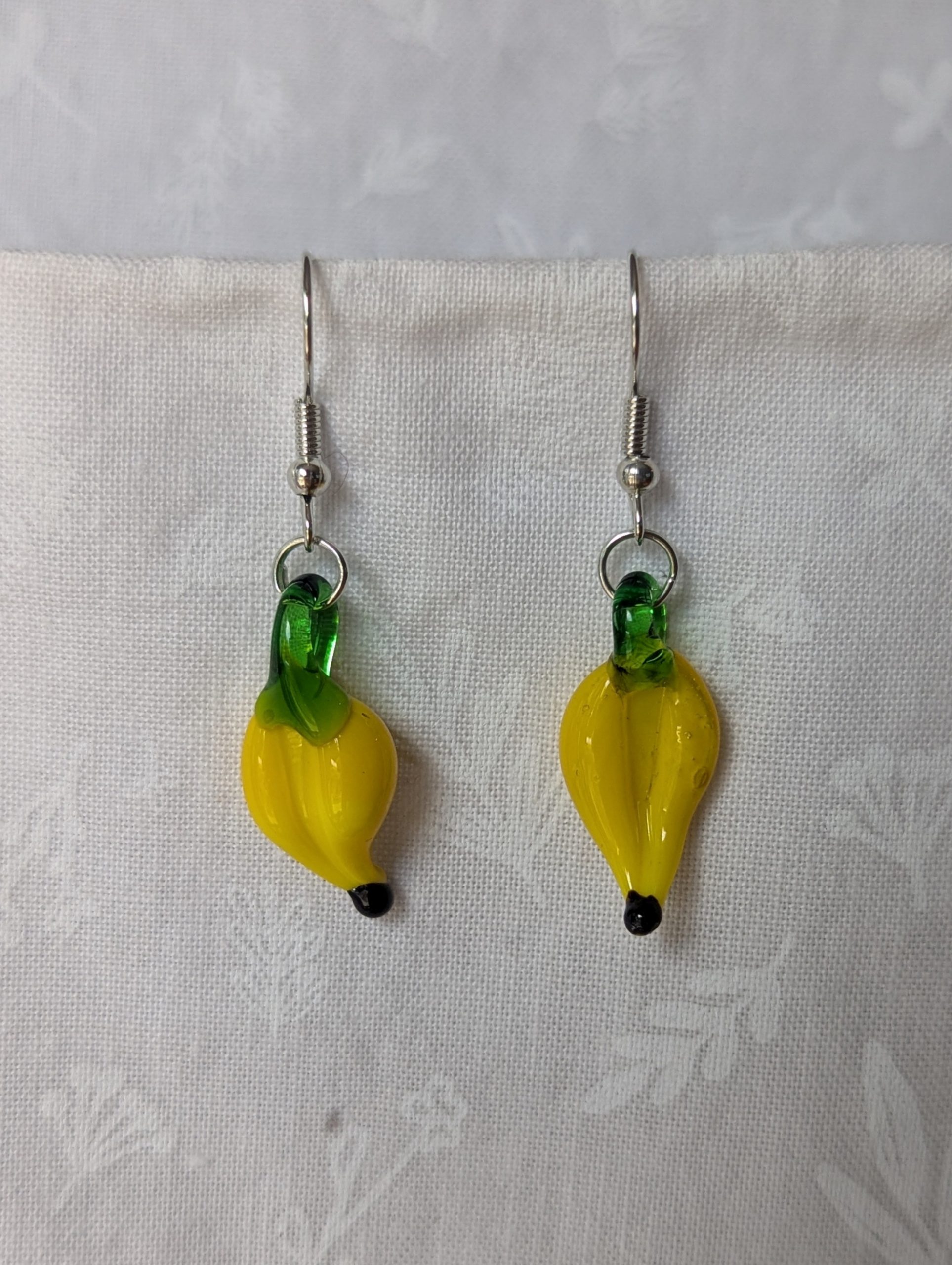 Handmade banana earrings with yellow glass bananas, green tops, and steel-colored hooks.
