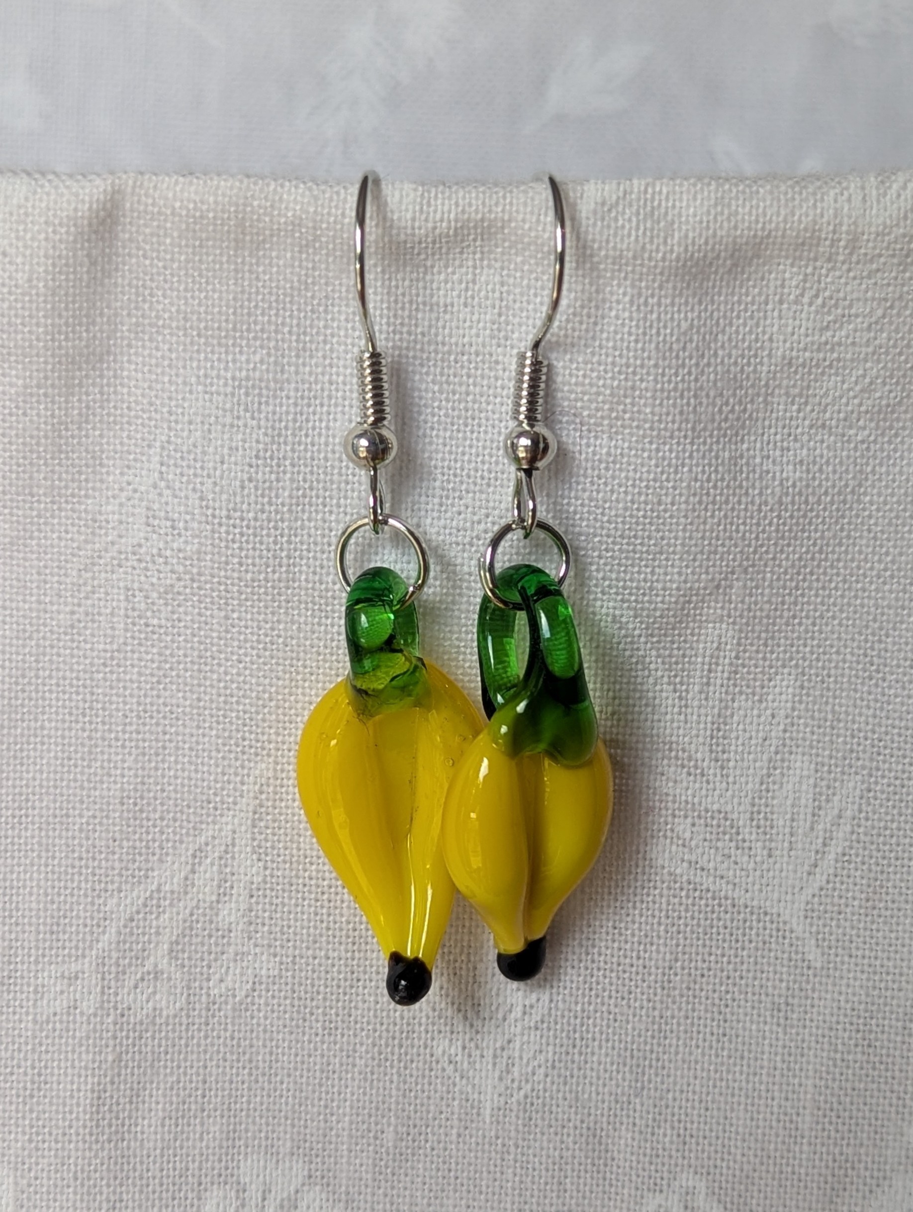 Handmade banana earrings with yellow glass bananas, green tops, and steel-colored hooks.