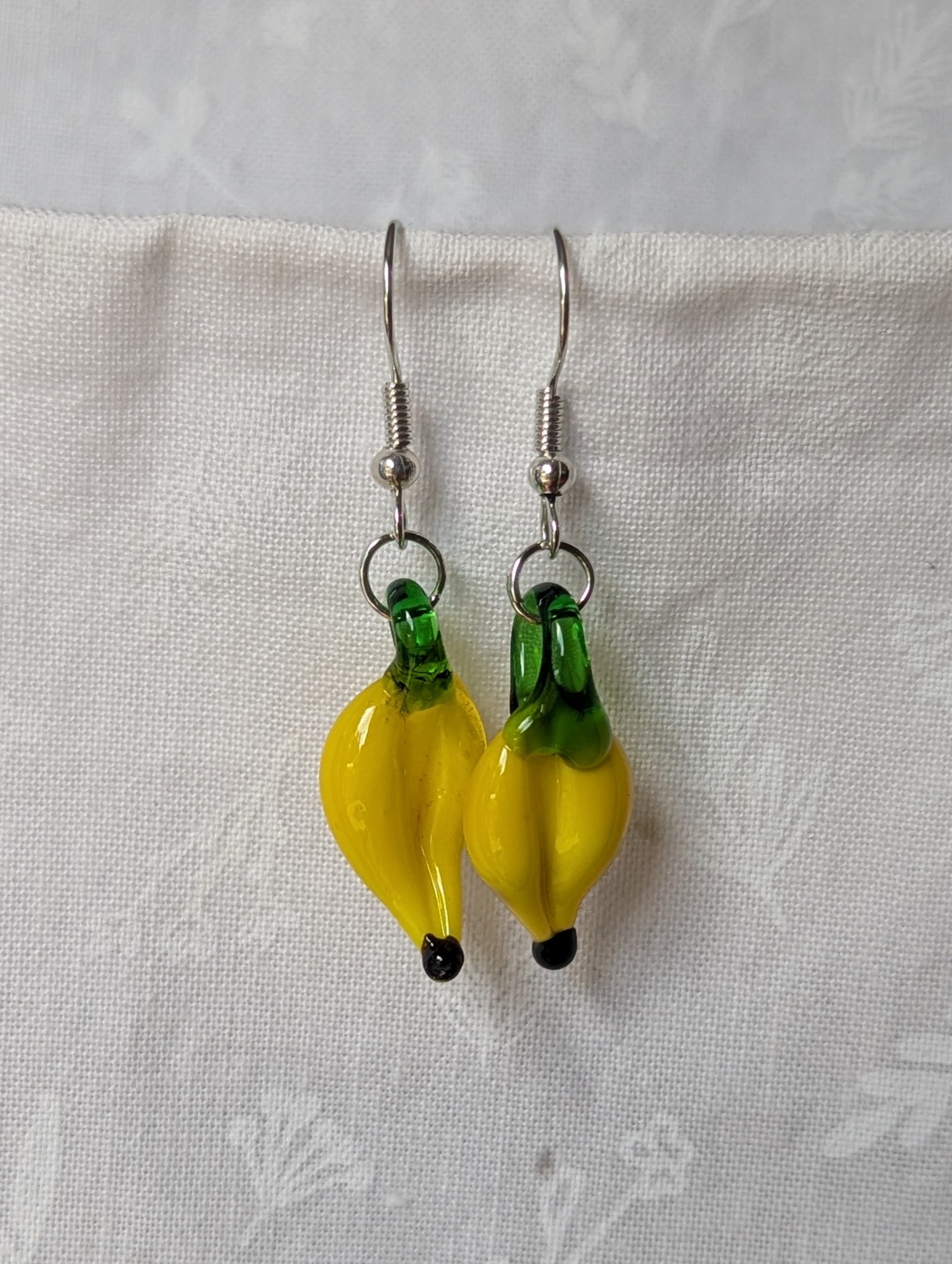 Handmade banana earrings with yellow glass bananas, green tops, and steel-colored hooks.