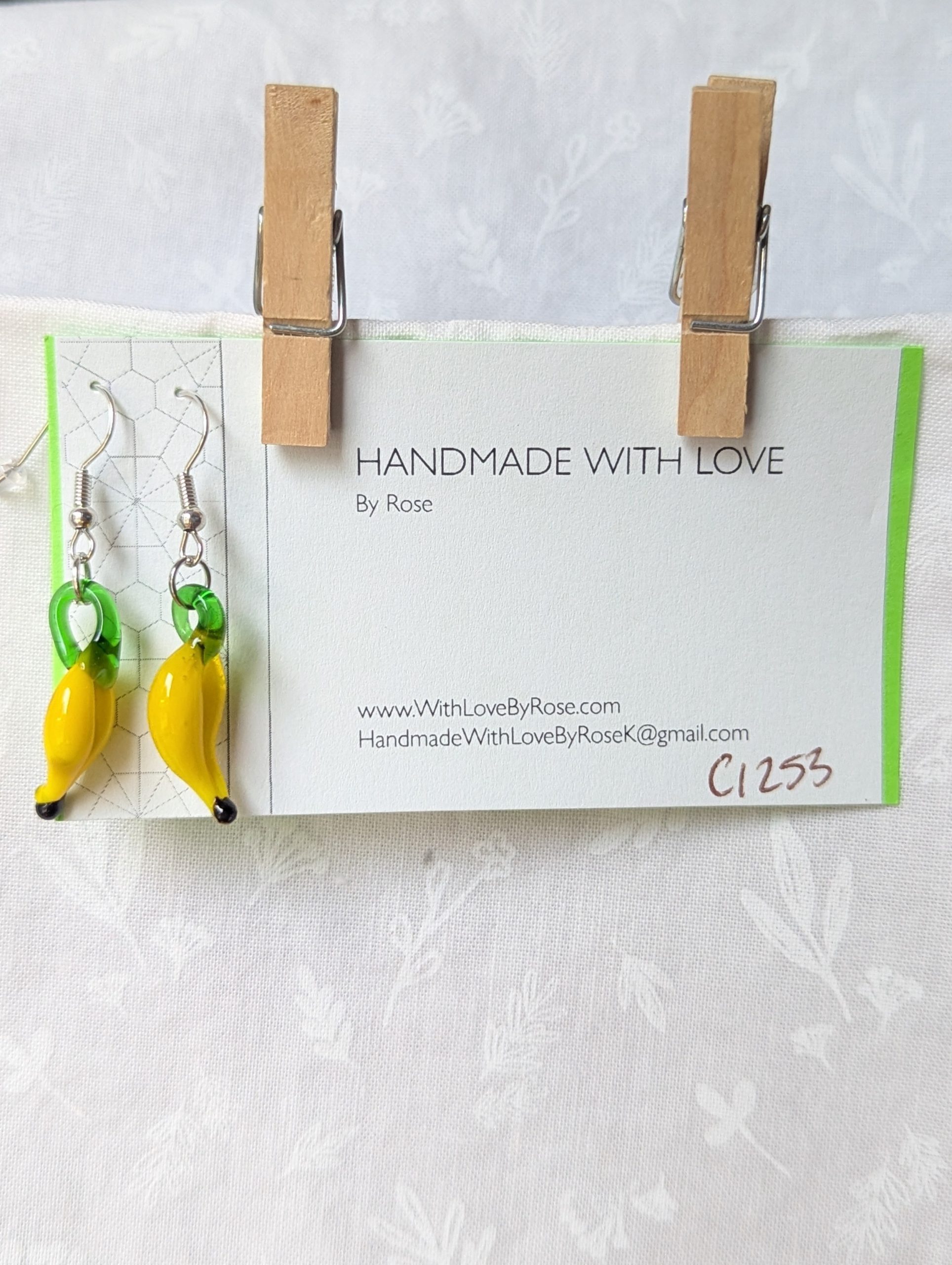 Handmade banana earrings with yellow glass bananas, green tops, and steel-colored hooks.