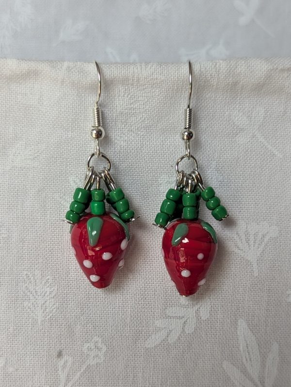 Handmade berry patch strawberry earrings with red and white polka-dotted glass strawberry beads, green seed bead accents, and steel-colored hooks.