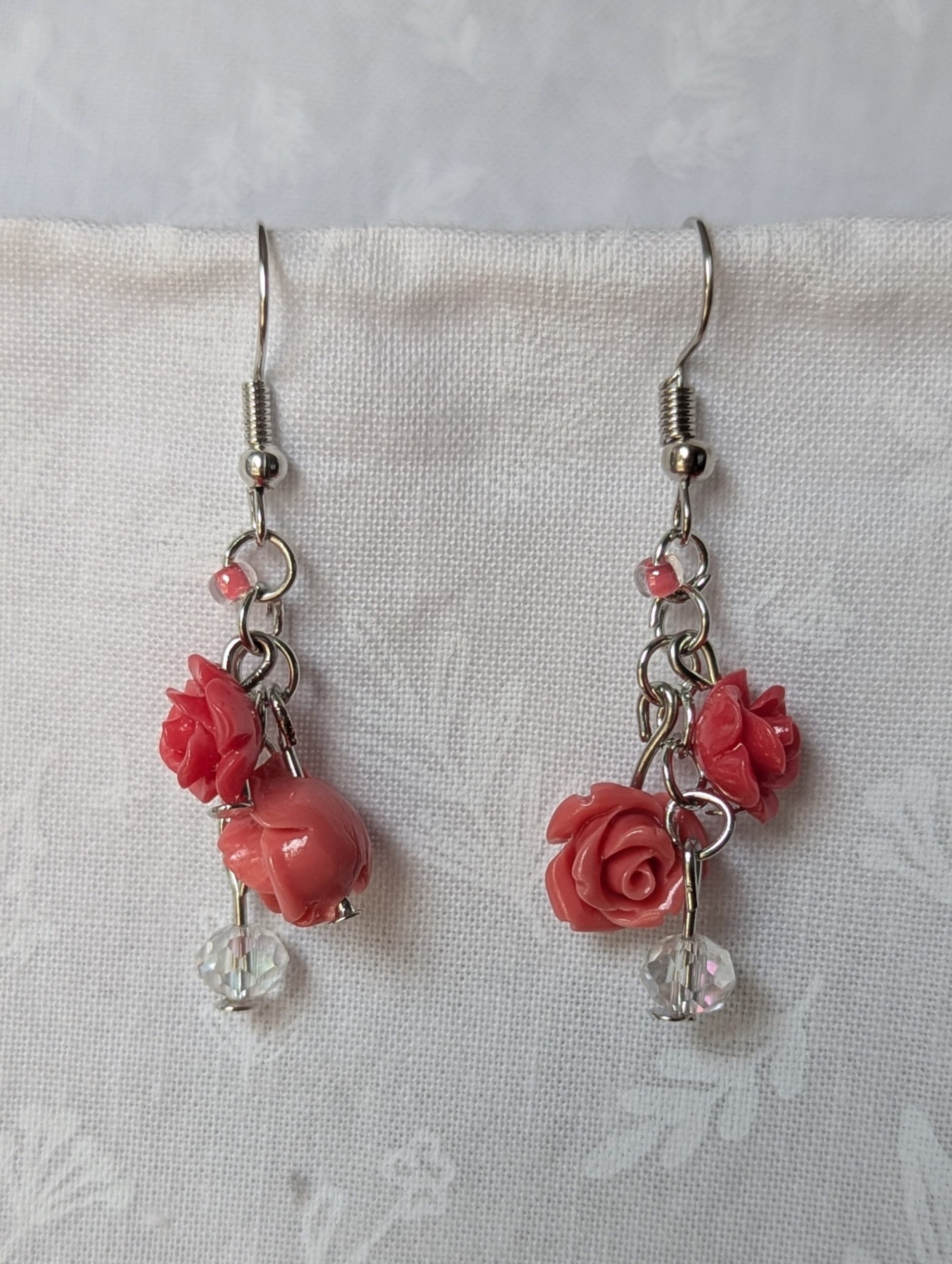 Handmade blooming rose earrings with coral and pink roses, glass seed beads, and crystal accents on steel colored hooks.