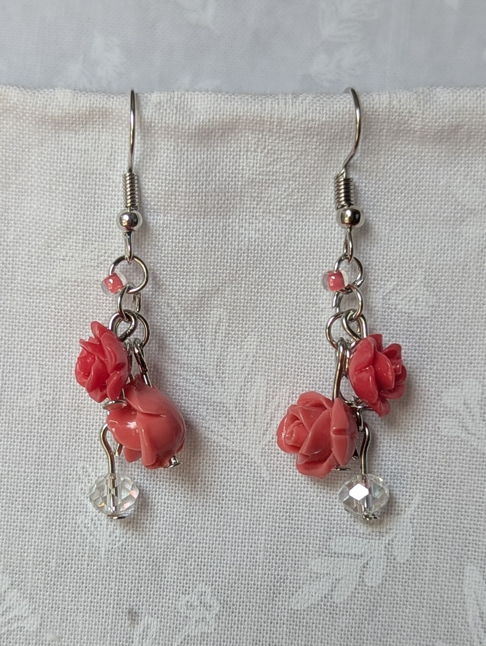 Handmade blooming rose earrings with coral and pink roses, glass seed beads, and crystal accents on steel colored hooks.