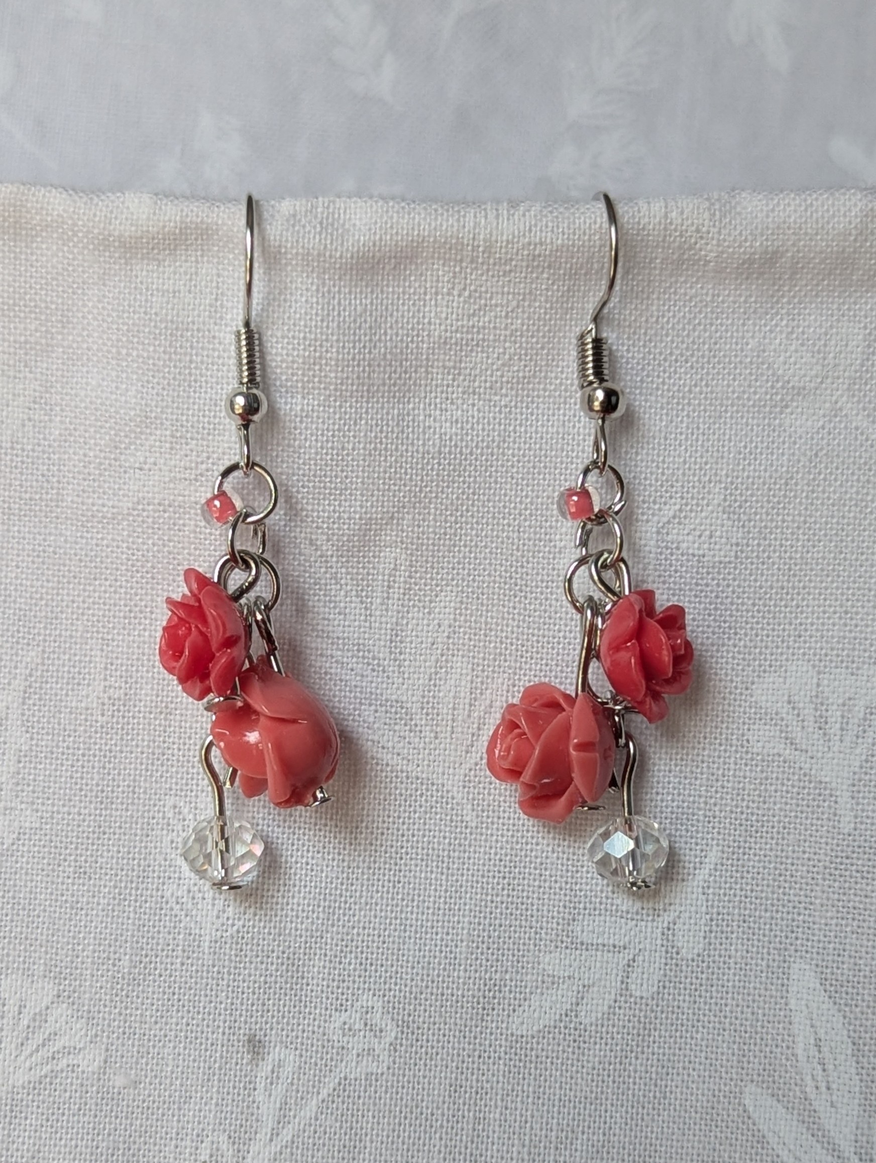 Handmade blooming rose earrings with coral and pink roses, glass seed beads, and crystal accents on steel colored hooks.
