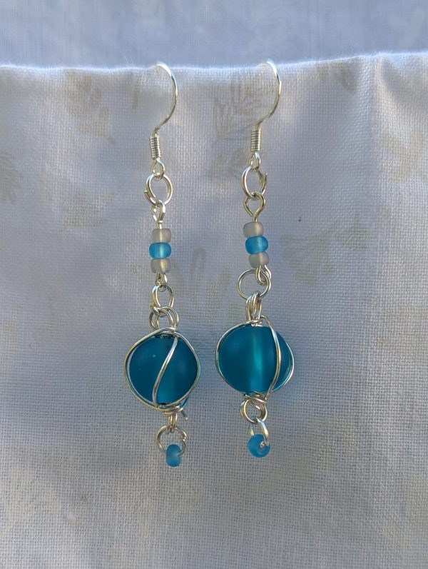 Handmade blue bead earrings with silver wire wrapping, blue and blue-gray seed beads, silver jump rings, and sterling silver hooks.