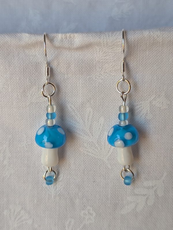 Handmade sky-blue mushroom earrings with glass toadstools, sky blue and white seed beads, and sterling silver hooks.