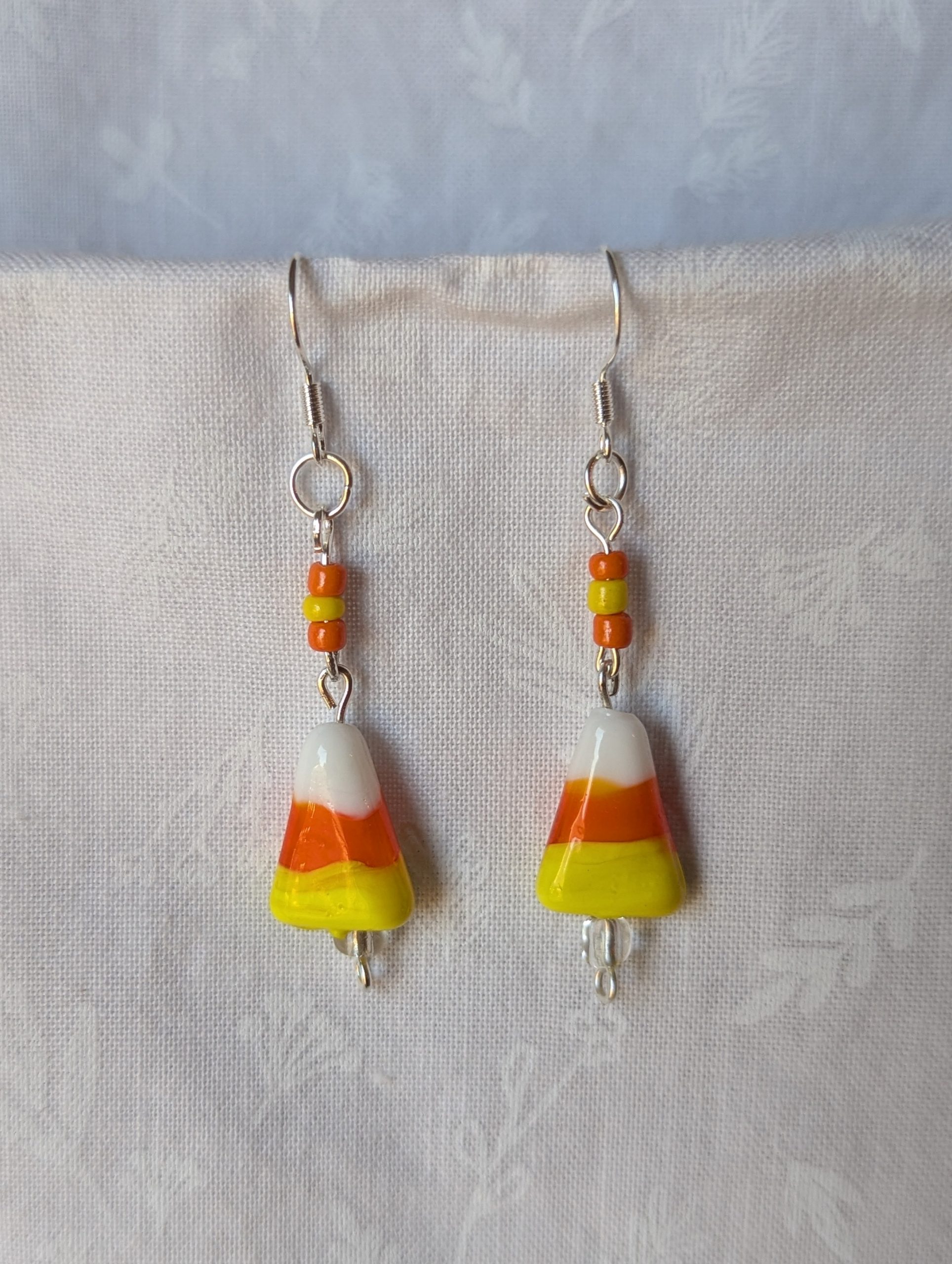 Handmade candy corn earrings with glass charms in yellow, orange, and white, accented by orange and yellow glass seed beads on sterling silver hooks.