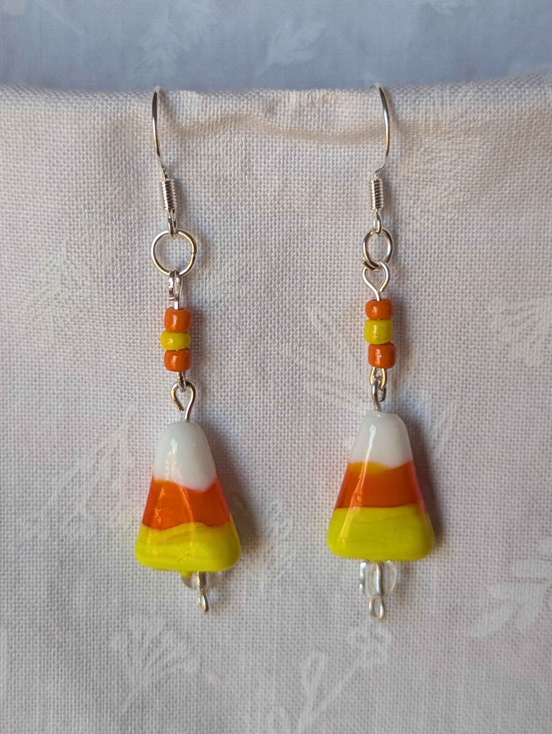 Handmade candy corn earrings with glass charms in yellow, orange, and white, accented by orange and yellow glass seed beads on sterling silver hooks.