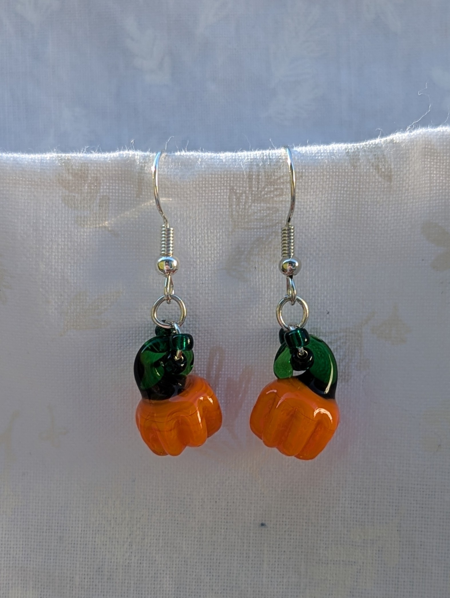 Handmade Halloween pumpkin earrings with amber-orange glass pumpkin beads, green accents, and steel-colored findings.
