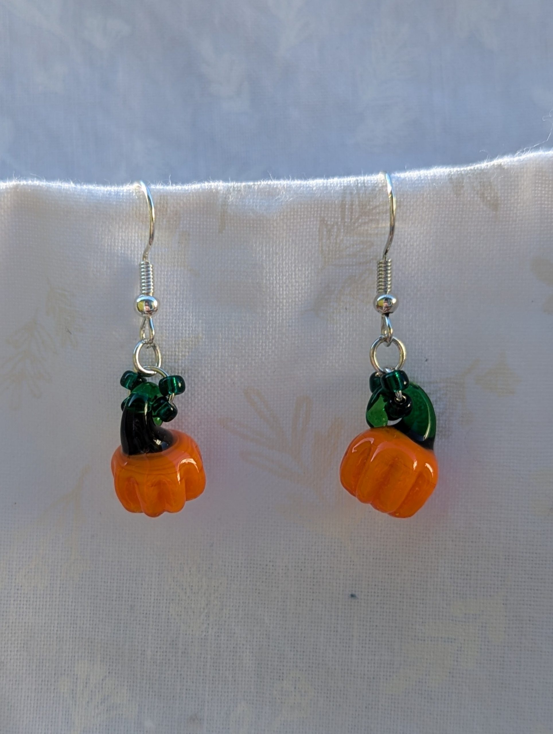 Handmade Halloween pumpkin earrings with amber-orange glass pumpkin beads, green accents, and steel-colored findings.