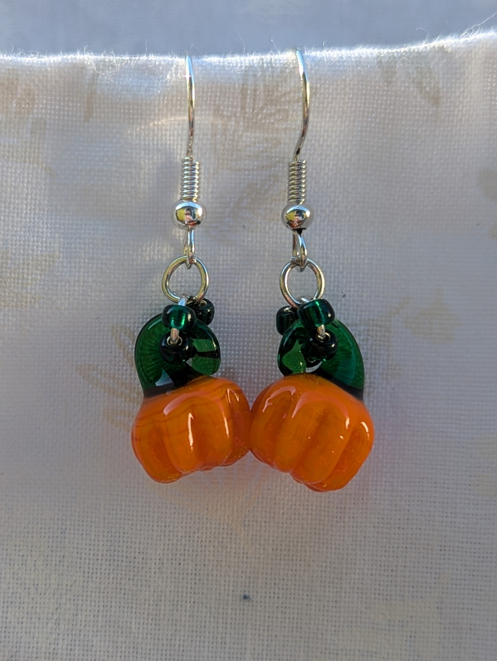 Handmade Halloween pumpkin earrings with amber-orange glass pumpkin beads, green accents, and steel-colored findings.