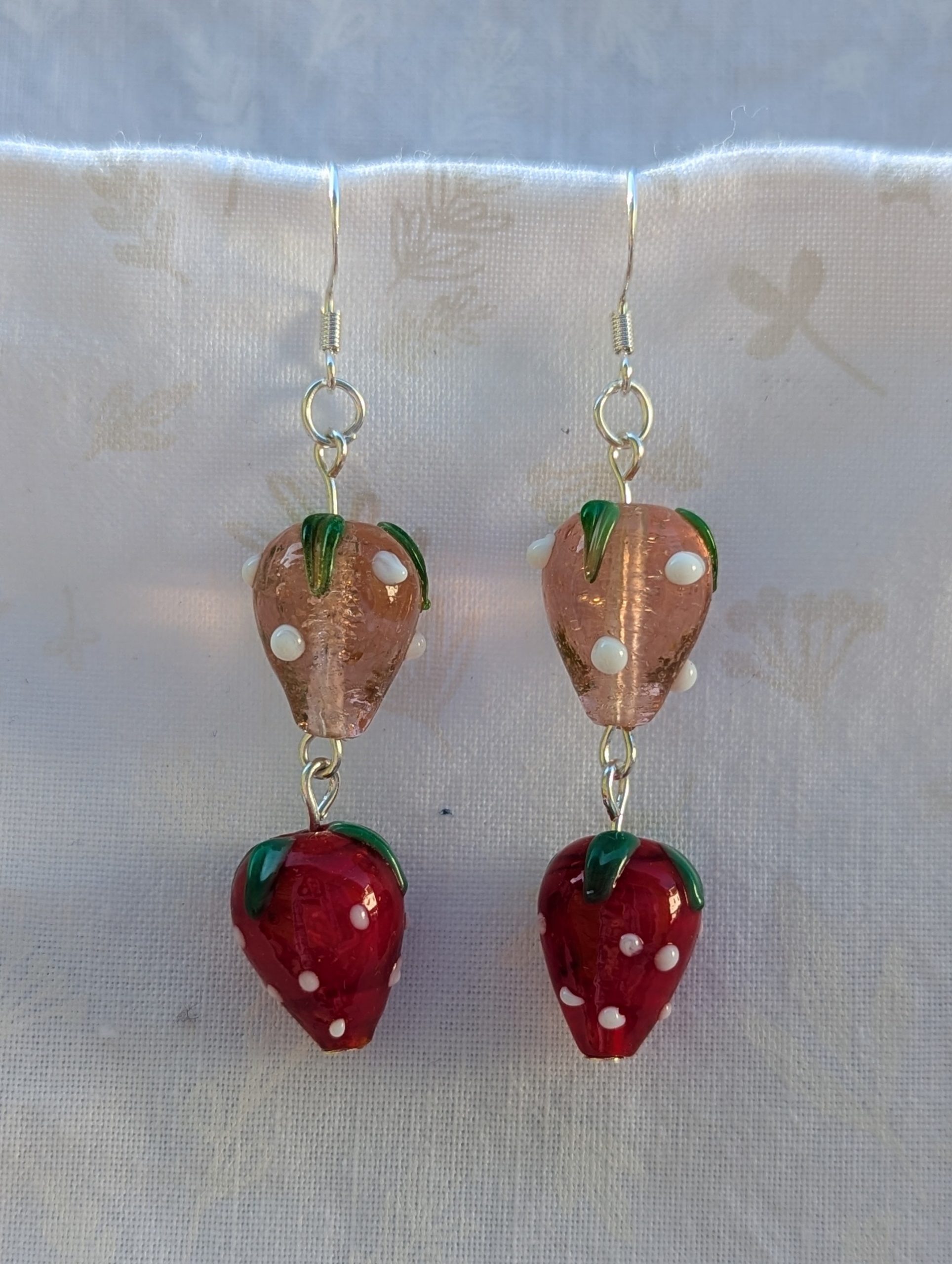 Handmade glass strawberry patch earrings with red, pale pink, green, and white details on sterling silver hooks.