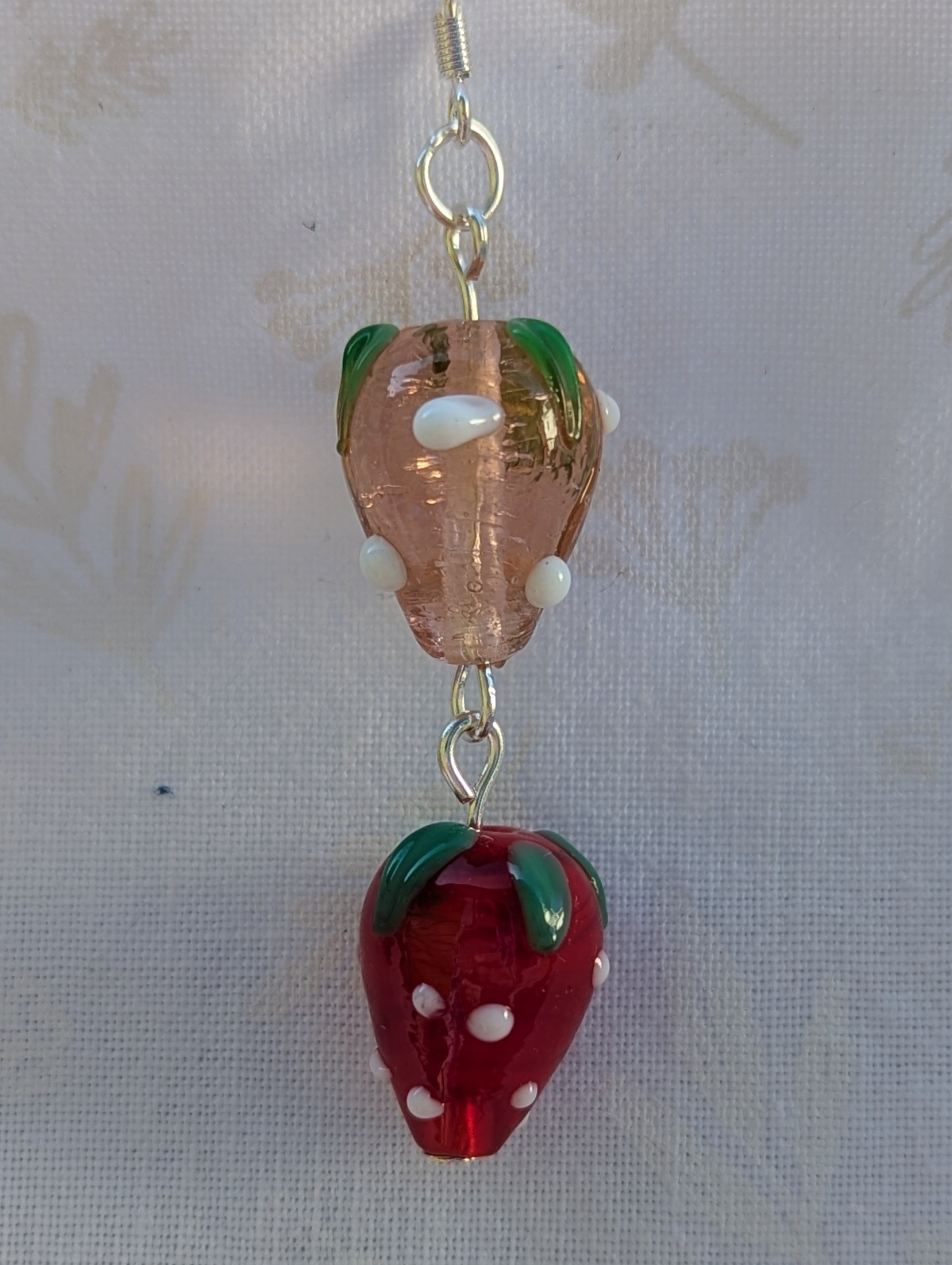 Handmade glass strawberry patch earrings with red, pale pink, green, and white details on sterling silver hooks.